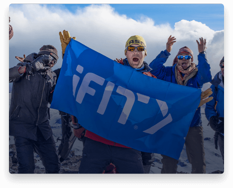 iFit Trainer Jake Norton standing with an iFit flag on Mount Kilimanjaro.