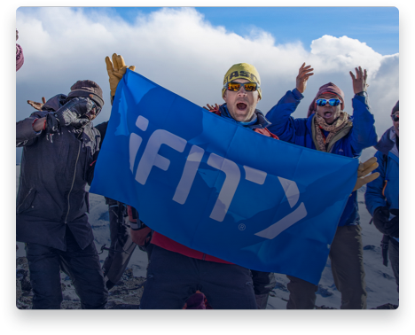 iFit Trainer Jake Norton standing with an iFit flag on Mount Kilimanjaro.